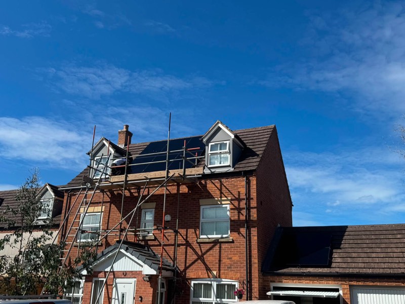 Solar panels being fitted to a three-storey brick house from scaffolding under a clear blue sky